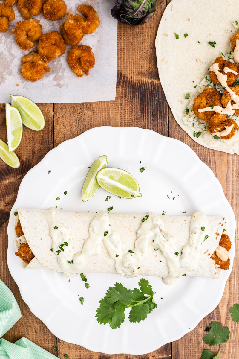 Overhead photo of a Low Carb Chipotle Shrimp Burrito on a white plate with more fried shrimp on a baking sheet close by.