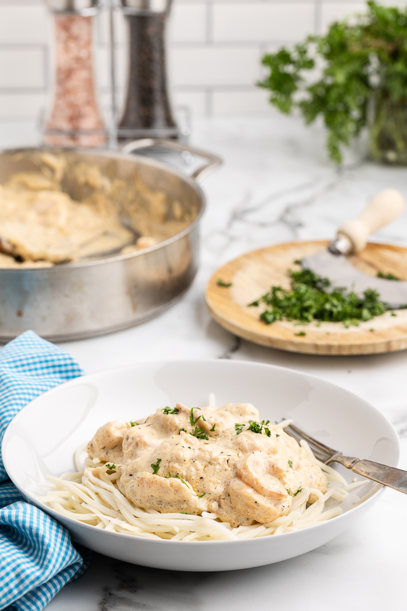 Photo of a white bowl filled with Keto Cajun Shrimp Alfredo with the pan holding the remaining Keto Cajun Shrimp Alfredo in the background.