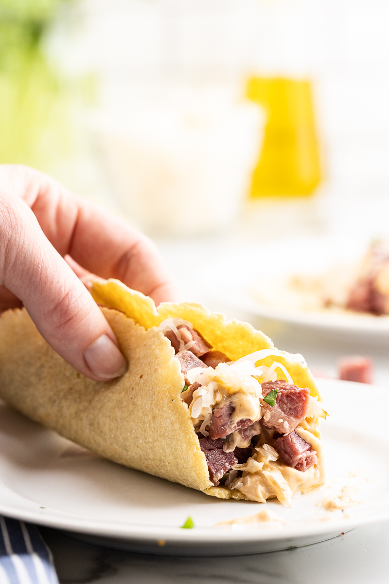 Closeup photo of someone holding a Keto Reuben Tacos over a white plate.