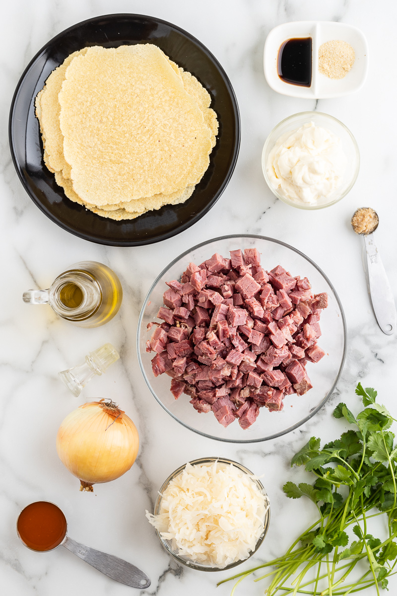 Overhead photo of the ingredients needed to make Keto Reuben Tacos on a marble counter.