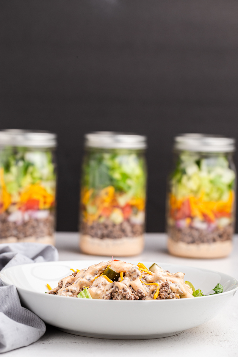 Big Mac Salad in a Jar poured into a white bowl for serving with 3 jars full of salad in the background.