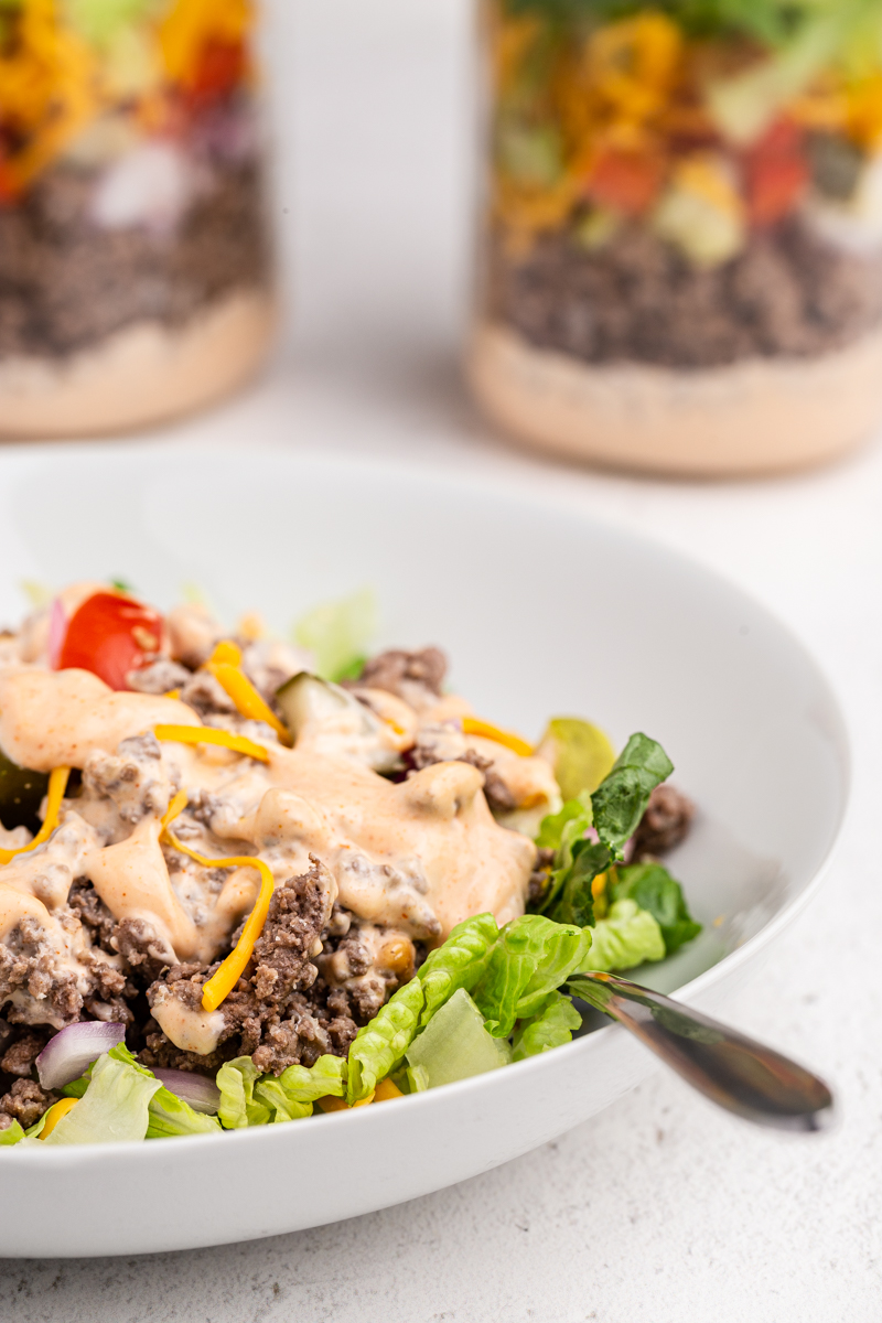 Close up photo of Big Mac Salad in a Jar poured into a white bowl with fork in the bowl as well.