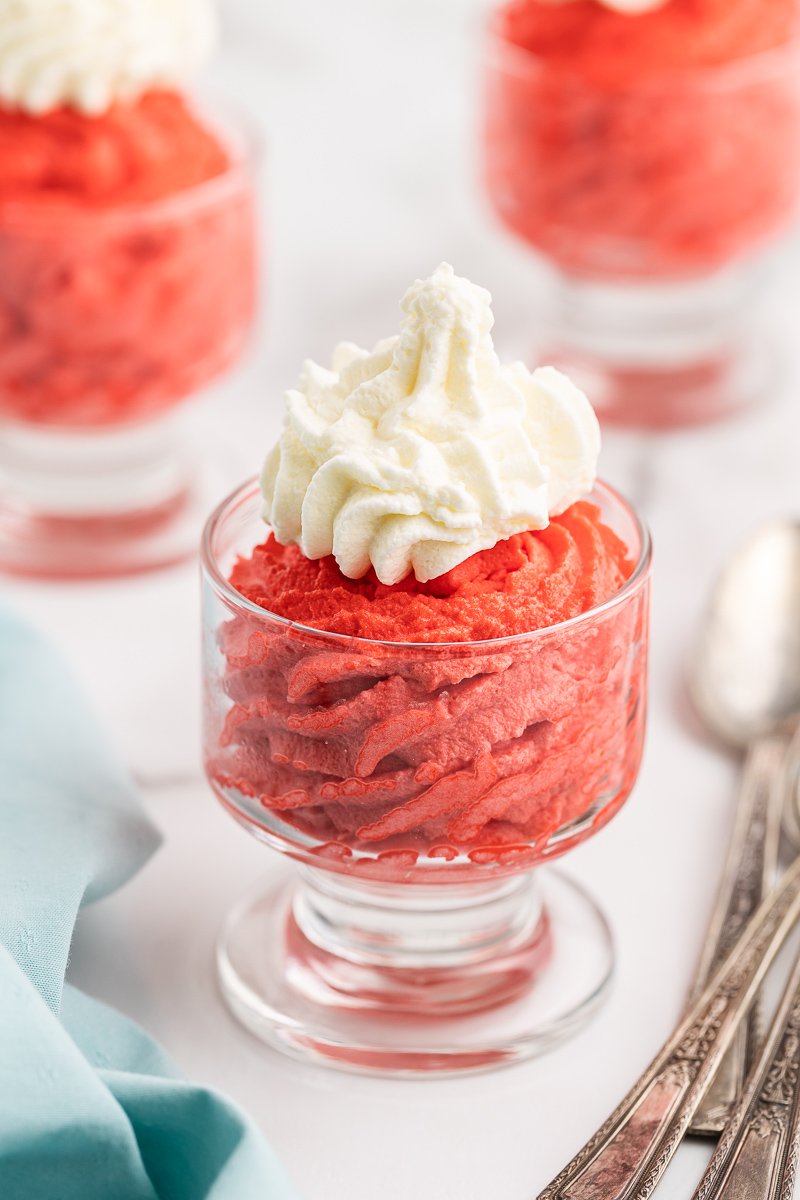 Three glass dessert cups filled with Keto Red Velvet Mousse and topped with whipped cream.