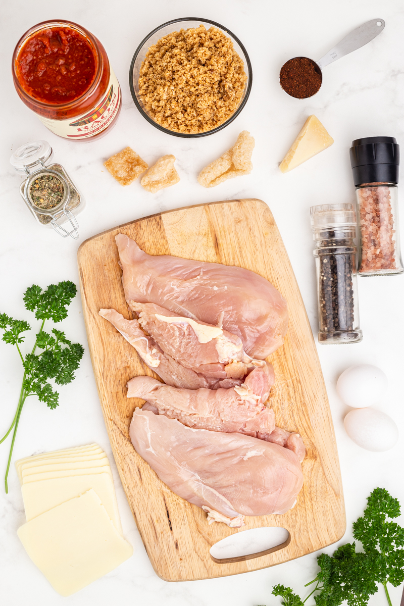 Overhead photo of the ingredients needed to make Keto Sheet Pan Chicken Parmesan on a white marble background.