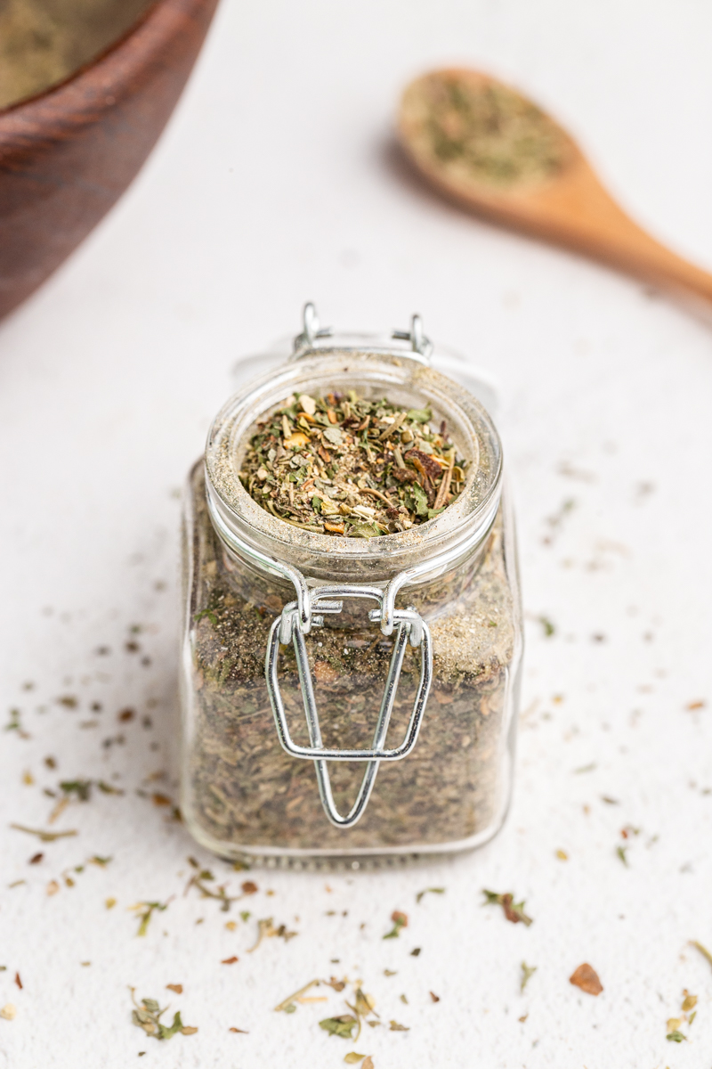 Homemade Italian seasoning in a glass jar on a white table.