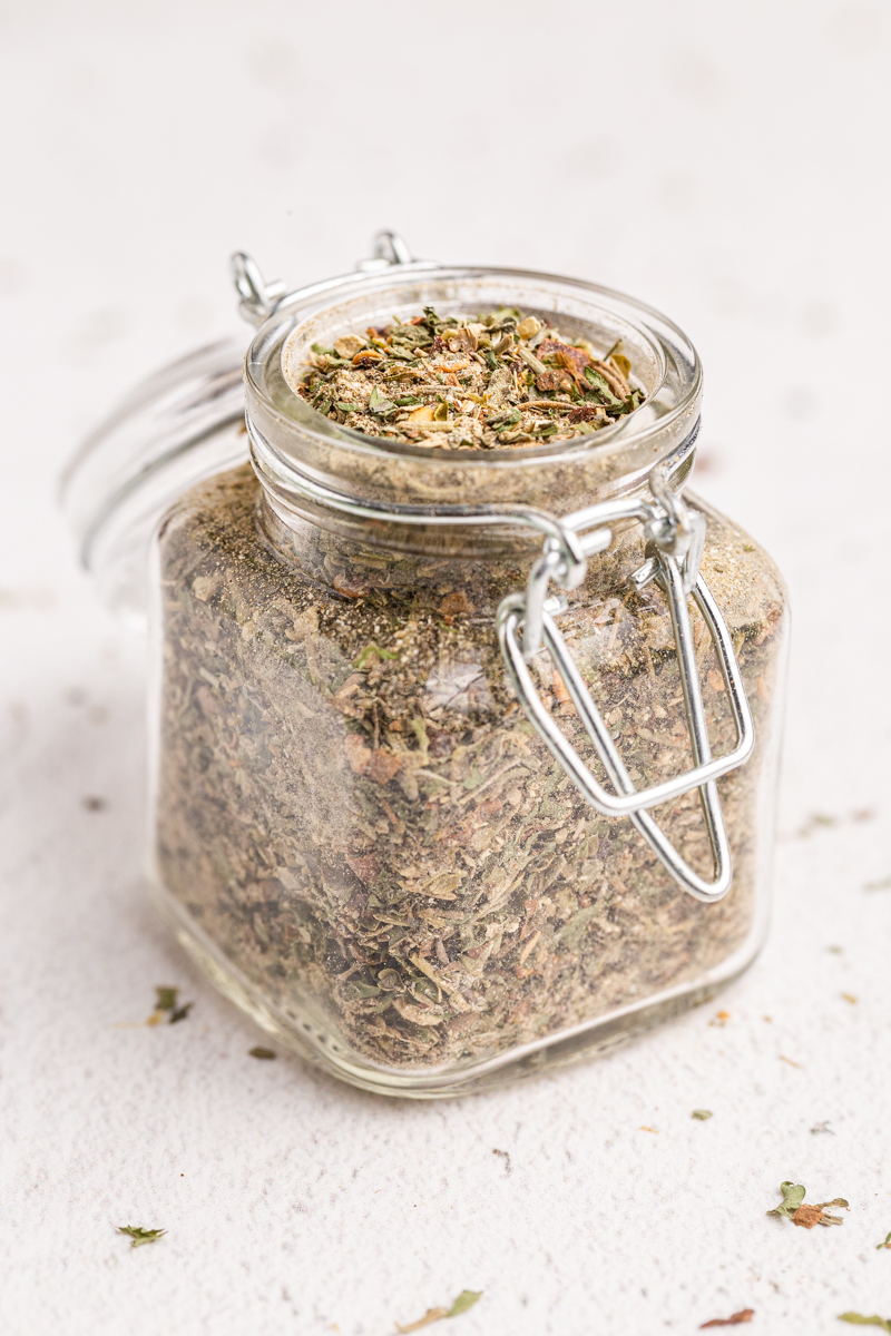 Homemade Italian seasoning in a glass spice jar on a white table.
