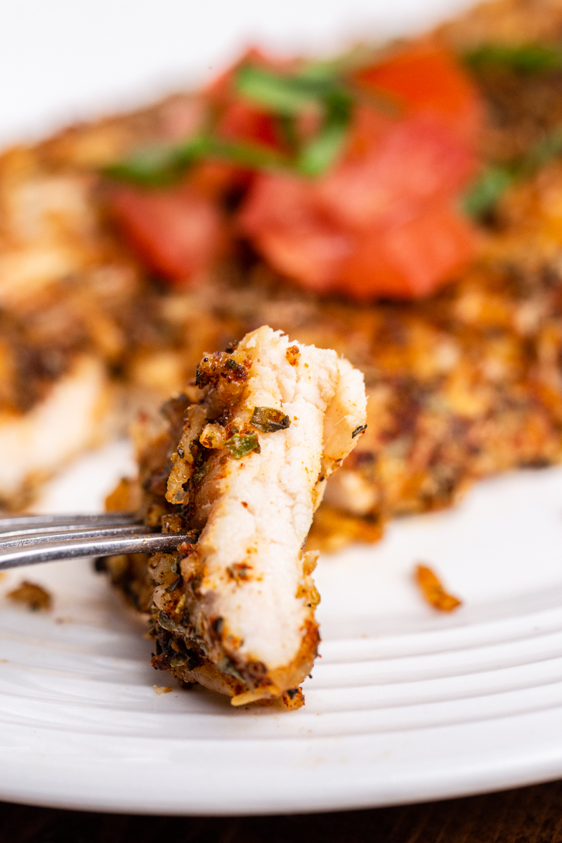 Very closeup photo of Keto Parmesan Crusted Chicken on a white plate with a bite on a fork.