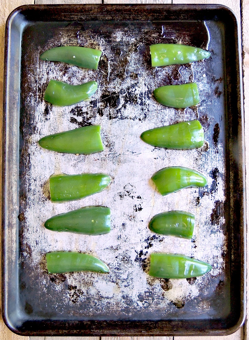 Overhead view of halved and seeded jalapenos on an old baking sheet.