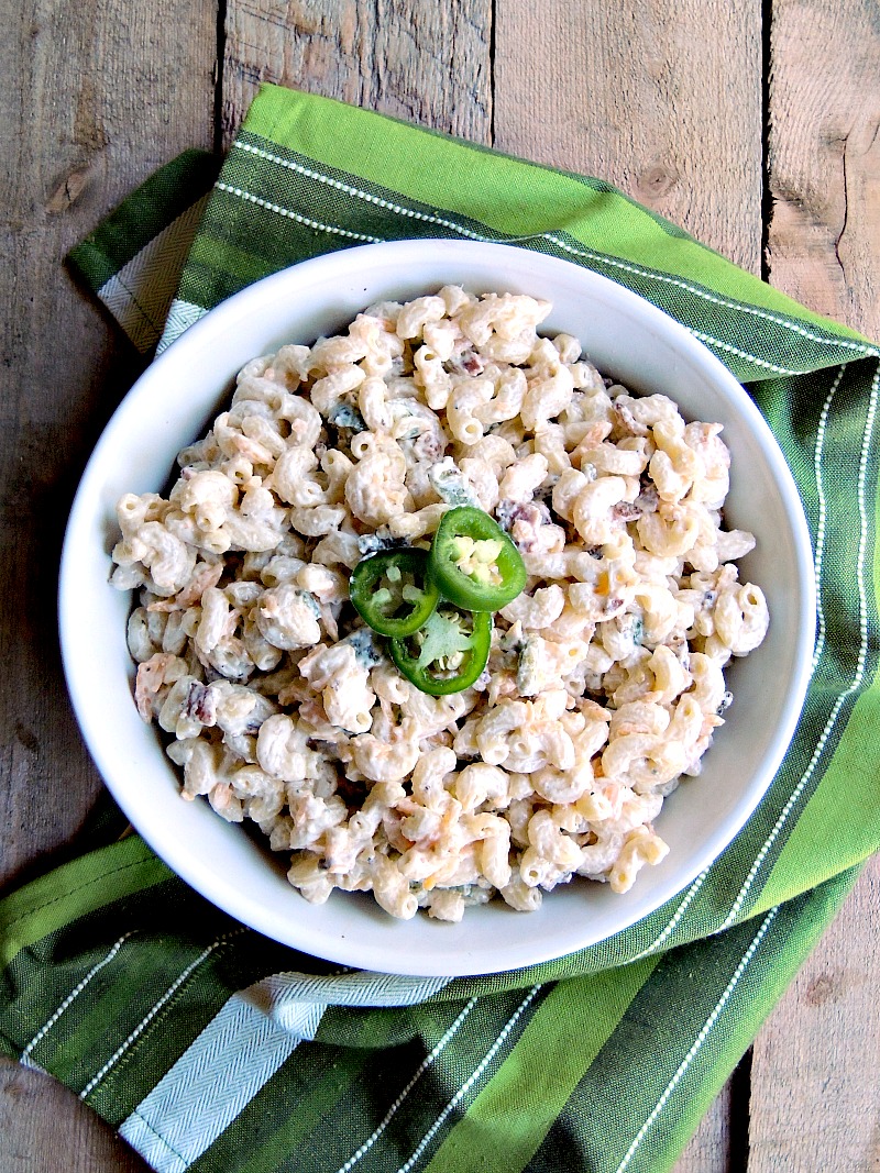 Overhead view of a bowl of jalapeno popper pasta salad on a wooden table with a green striped kitchen towel.