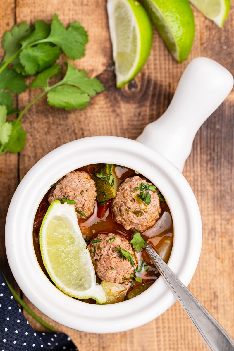 Closeup overhead photo of Keto Albondigas (Meatball) Soup with a lime wedge and spoon in the bowl.