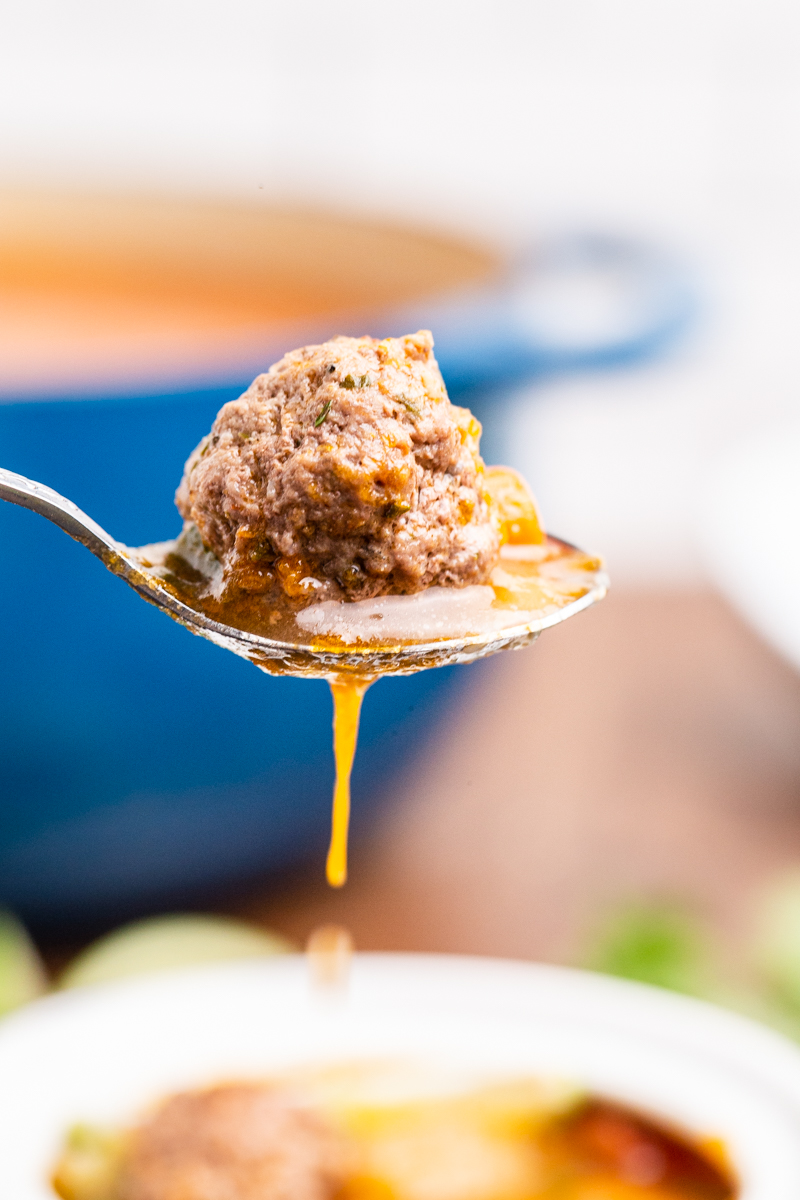 Close up photo of a meatball from Keto Albondigas (Meatball) Soup on a spoon with some of the broth drizzling down.