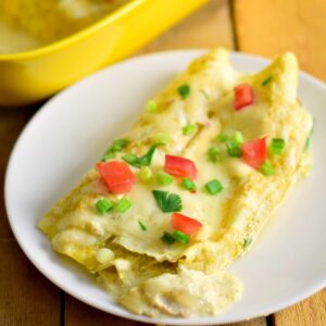 Creamy keto green chile chicken enchiladas on a white plate topped with chopped tomato, green onions, and cilantro.