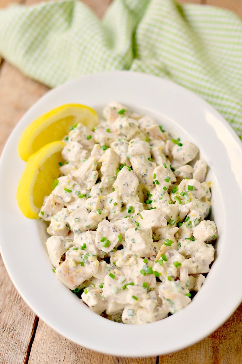 Lemon herb chicken salad in a white dish with lemon wedges.