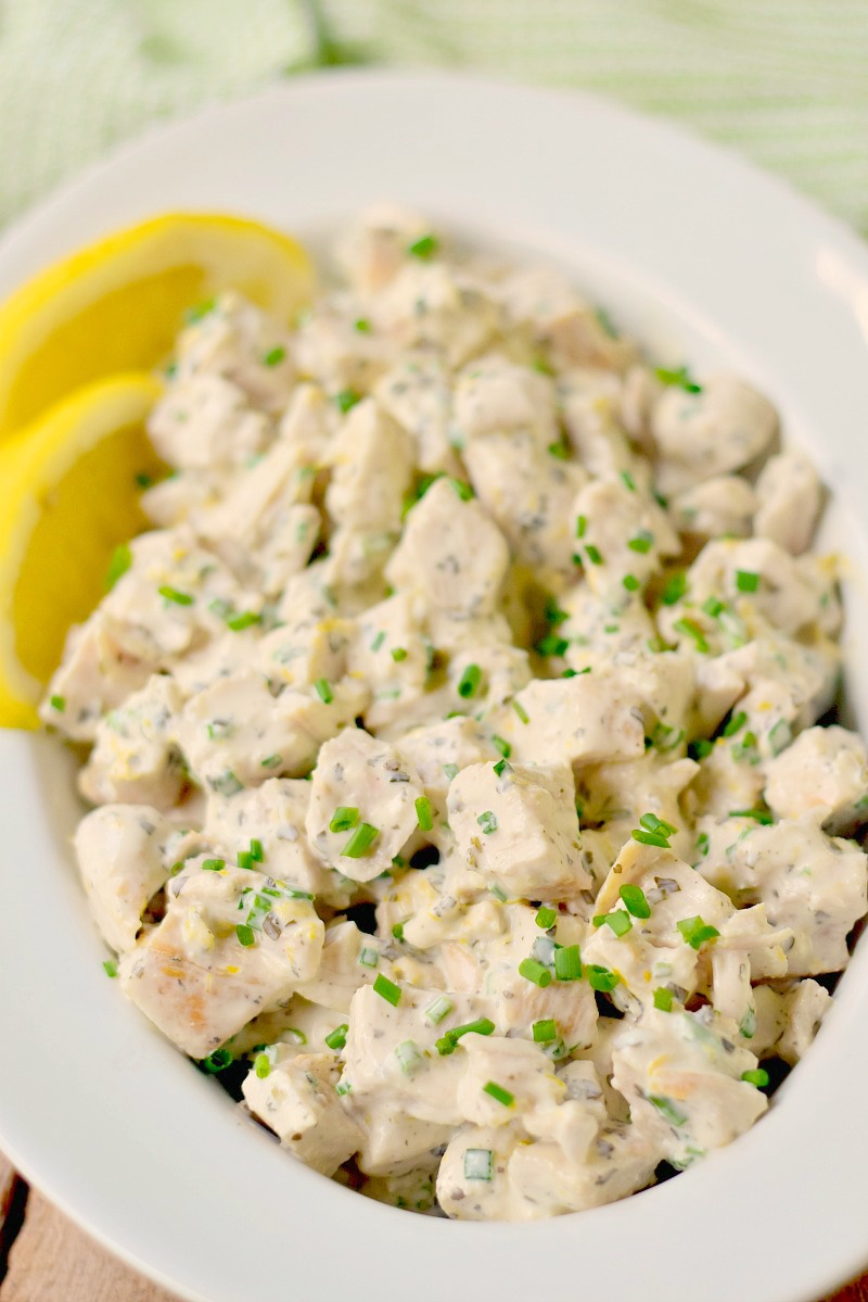 Lemon herb chicken salad in a white swerving dish on a wooden table.