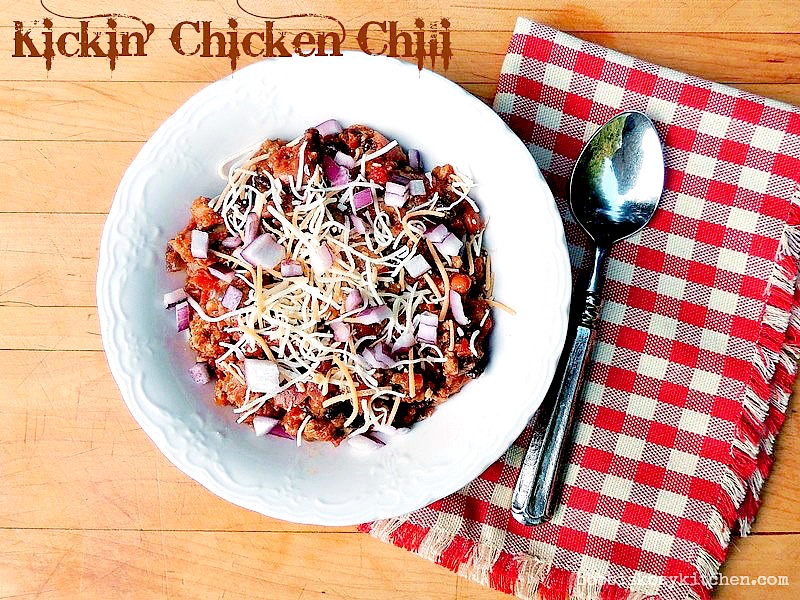 Kickin' Chicken Chili in a white bowl on a wooden background with a red and white checkered napkin.
