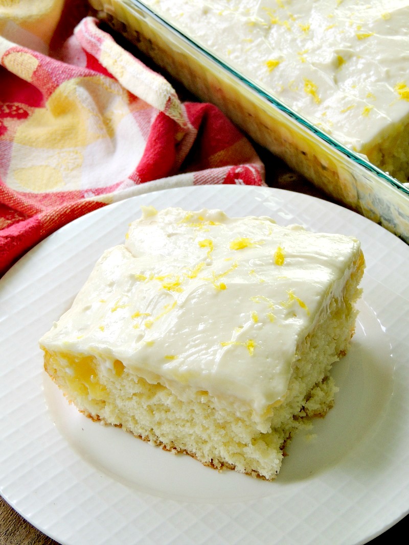Sunshine Lemon Poke Cake in a glass dish on a wooden table with a yellow and red plaid table runner.