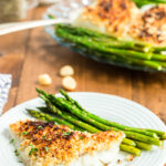 Oven Baked Coconut Macadamia Nut Crusted Cod on a white plate with asparagus.
