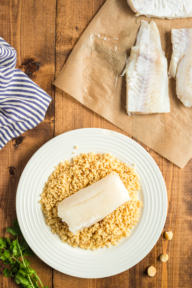 Cod filet on a plate full of macadamia nut crumbs.