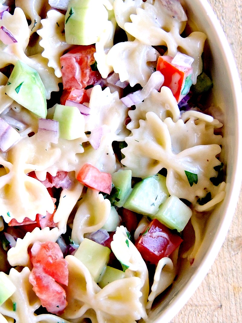 Mediterranean Pasta Salad in a bowl with a green striped hand towel in the background on a wooden background