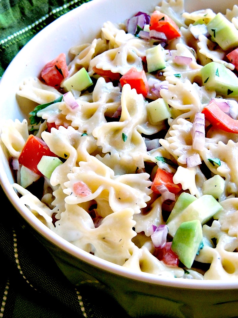 A tantalizing close-up of Mediterranean Pasta Salad in a bowl, showcasing vibrant colors and textures. The salad features a colorful mix of fresh vegetables, flavorful dressing, and perfectly cooked pasta. A green striped hand towel provides a stylish backdrop, while the rustic wooden surface adds a touch of warmth to the composition.