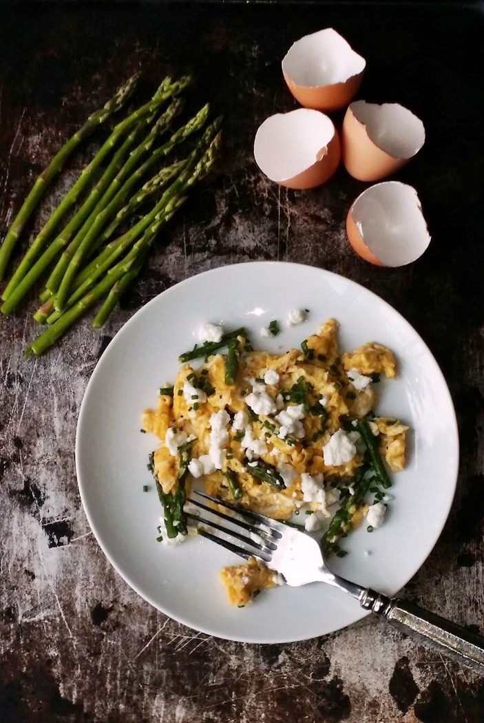 Overhead photo of Perfectly Scrambled Eggs with Asparagus and Goat Cheese on a white plate with a metal background.