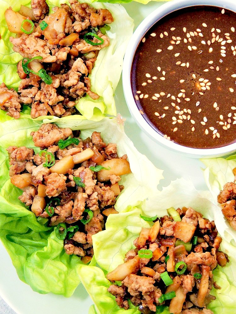 Close up of Copycat PF Chang’s Chicken Lettuce Wraps on a white serving platter with dipping sauce in a white bowl.