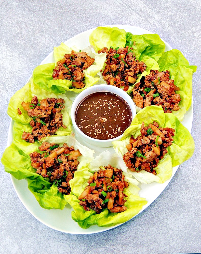 Copycat PF Chang’s Chicken Lettuce Wraps on a white serving platter with dipping sauce in a white bowl on a light blue background.