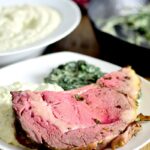 a slice of medium rare Rib Roast with Garlic Herb Butter on a white plate with mashed cauliflower and creamed spinach.