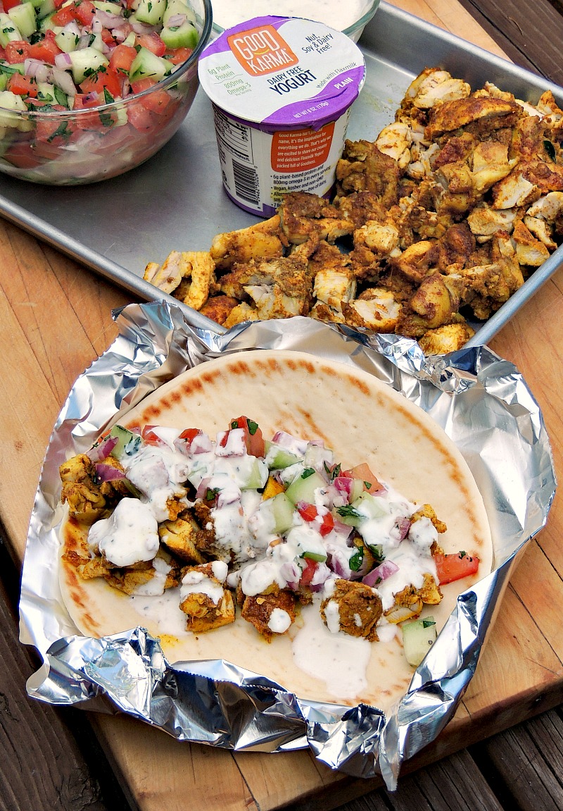 Ingredients for a Sheet Pan Chicken Shawarma sandwich on a metal baking sheet with an open face Sheet Pan Chicken Shawarma sandwich on foil to the side.