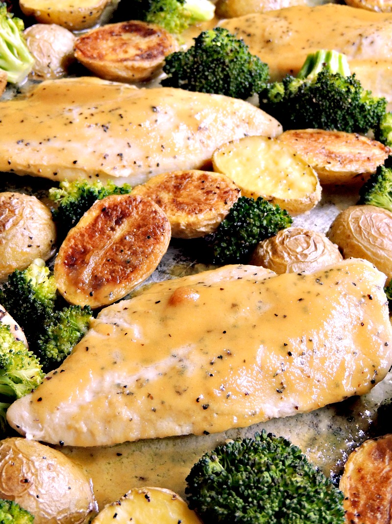 Close up of honey mustard chicken with broccoli and potatoes on a sheet pan.