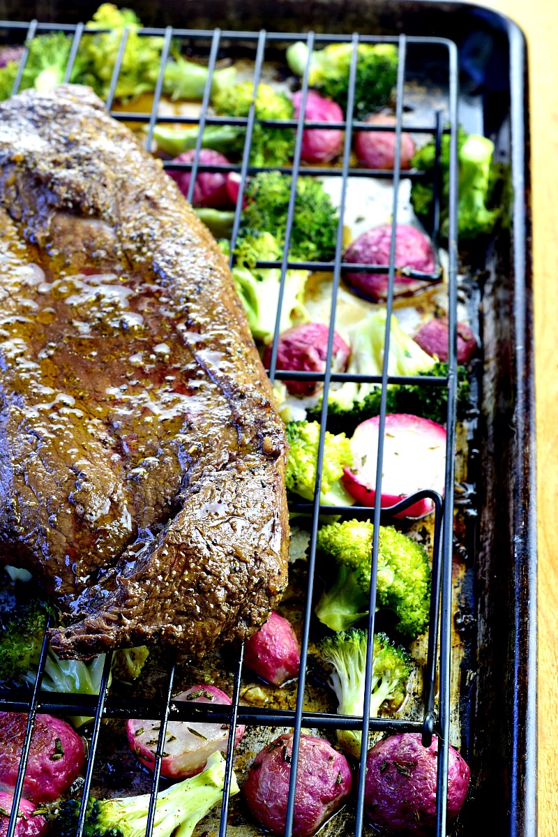Cooked steak on a wire rack over broccoli and radishes on a sheet pan.