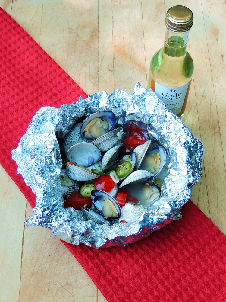 Spicy Grilled Clams in Foil on a wooden cutting board with a red fabric runner.
