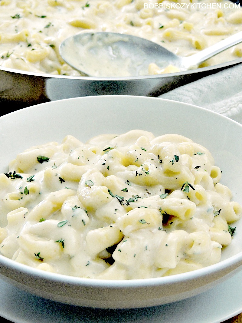 Closeup of keto stovetop white mac and cheese in a white bowl with the pot of remaining mac and cheese in the background.