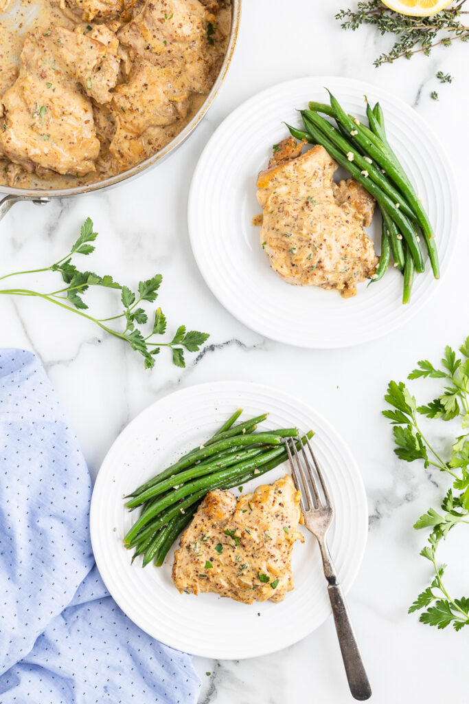 Overhead photo of two white dinner plates with Creamy Mustard Chicken and green beans on them.