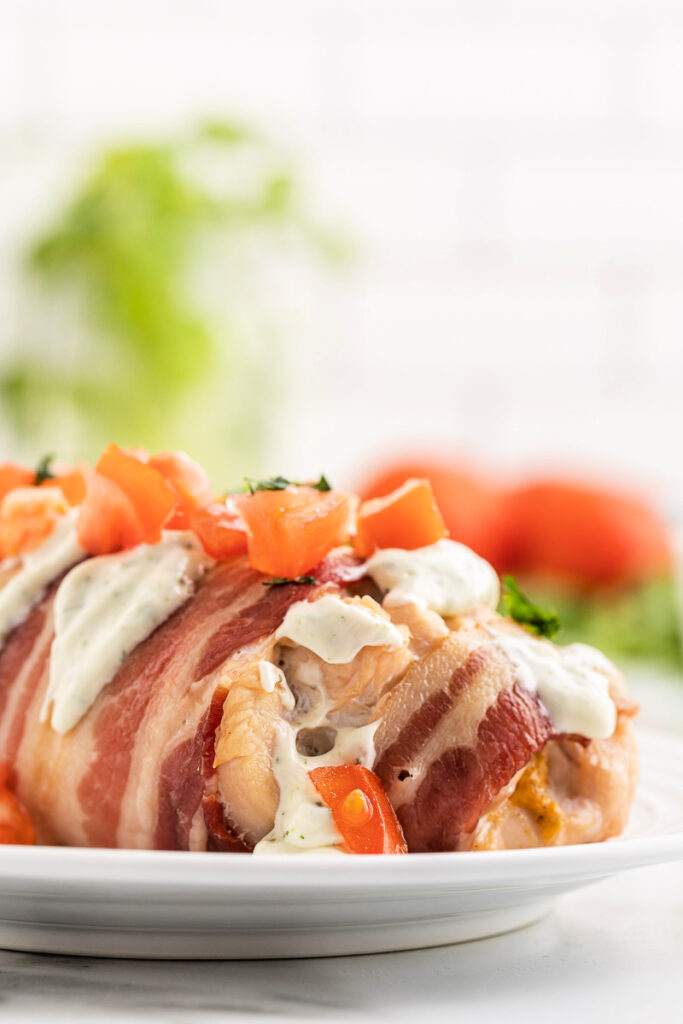 Closeup of a serving of Bacon Wrapped Jalapeno Popper Chicken on a white plate.