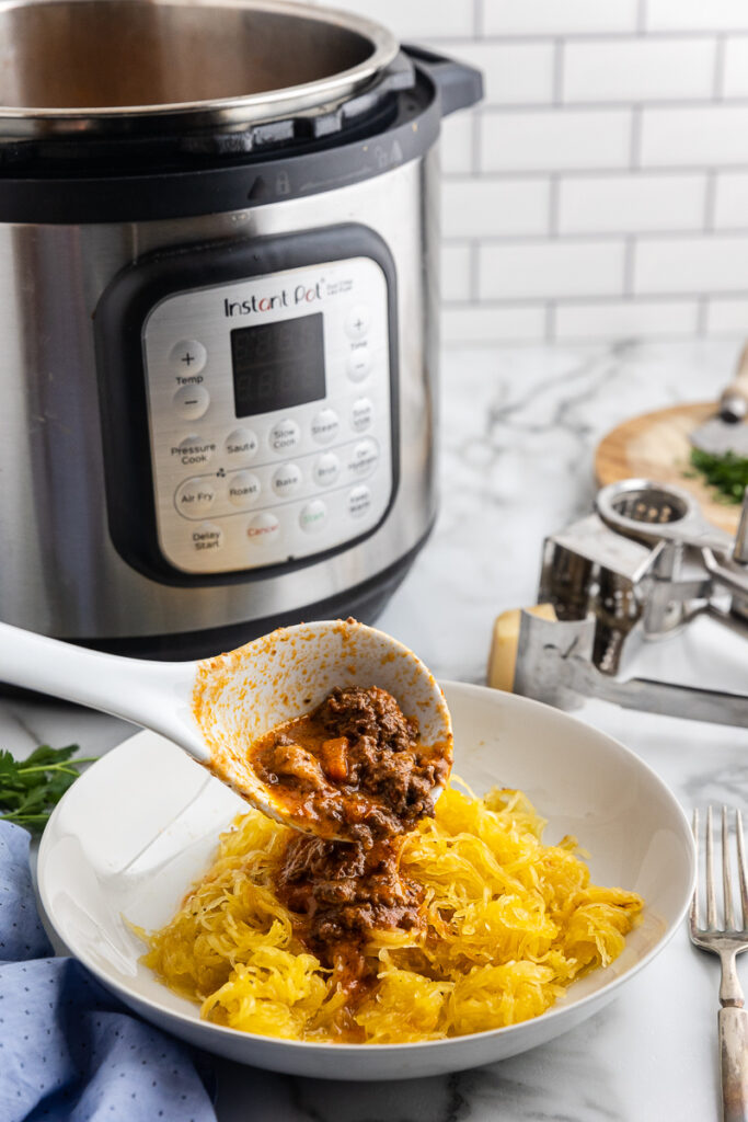 Photo of Instant Pot Bolognese Sauce (Low Carb) being poured from a ladle onto a bowlful of spaghetti squash noodles.