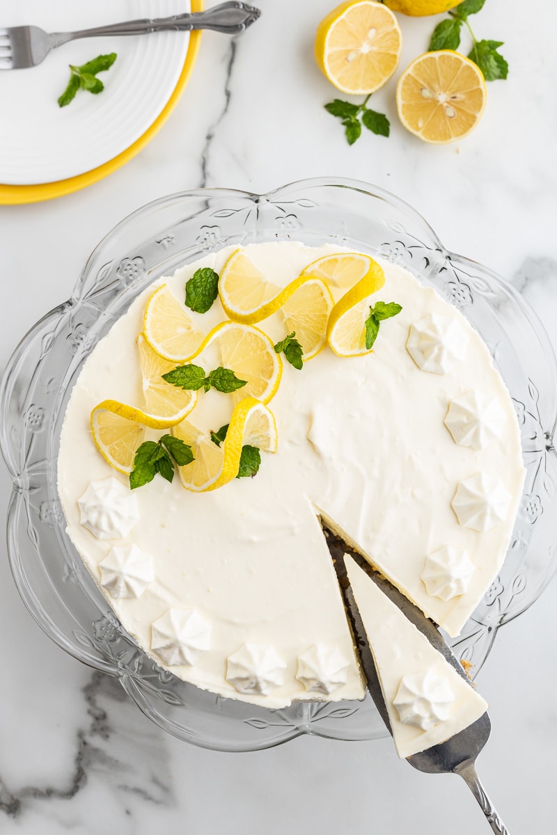 Overhead view of keto no-bake lemon cheesecake on a glass cake pan with a slice cut out.