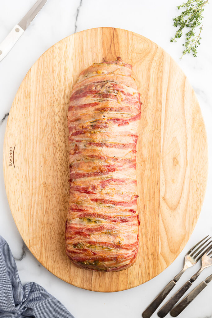 Overhead photo of a bacon wrapped honey mustard glazed pork loin on a wooden cutting board.