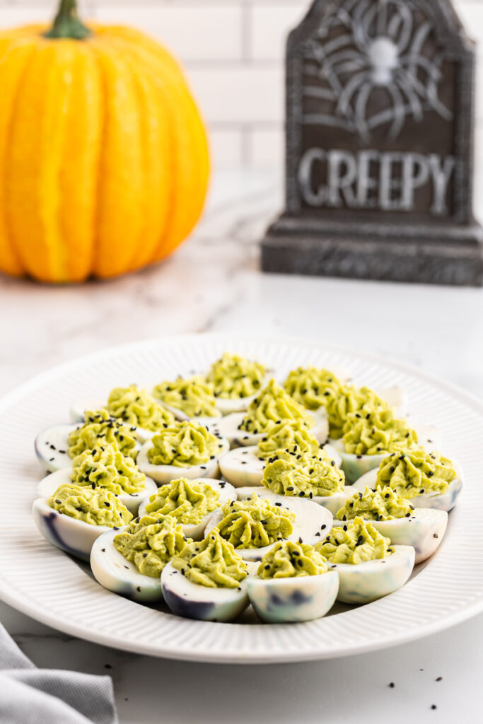 Halloween Deviled Eggs on a white platter with a tombstone in the background on a white marble counter.