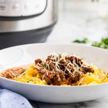 Low carb instant pot bolognese sauce over spaghetti squash in a white bowl with an instant pot in the background.