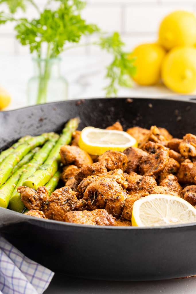 Lemon garlic chicken and asparagus spears in a cast iron skillet with lemon slices as garnish.