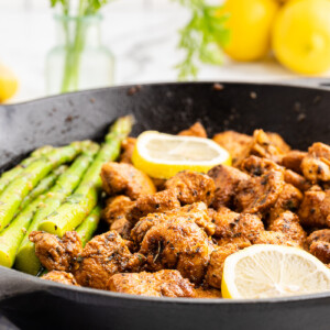 Lemon garlic chicken bites with asparagus in a skillet with a lemon wedge.