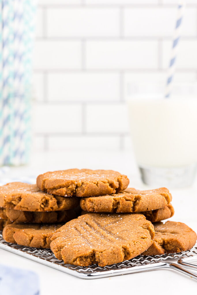 Several Keto Peanut Butter Cookies on a metal cooling rack with a glass of milk in the background.
