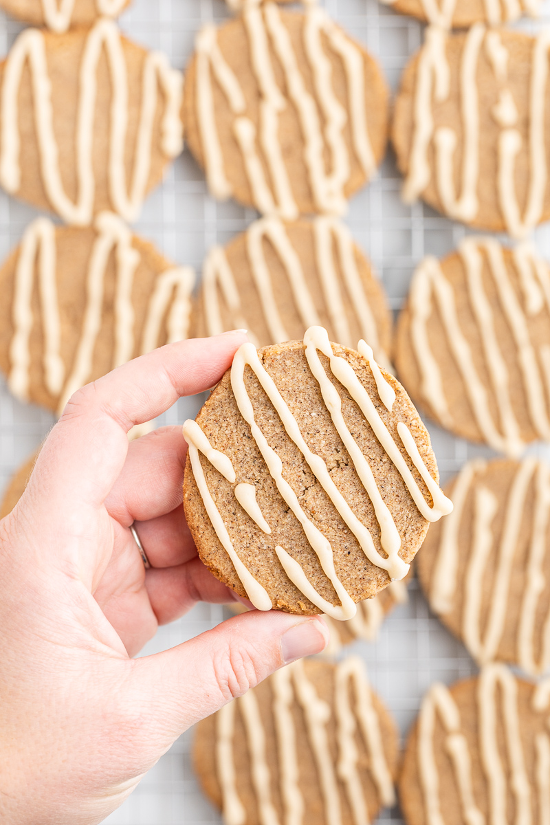 Image shows a white hand holding a keto chai sugar cooking about several cookies on a cooling rack.