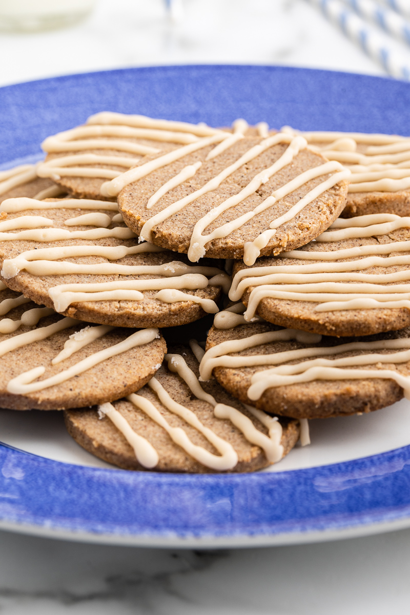 Image shows several keto chai sugar cookies stacked on a plate with a blue rim. The plate is sitting on a white marble counter.
