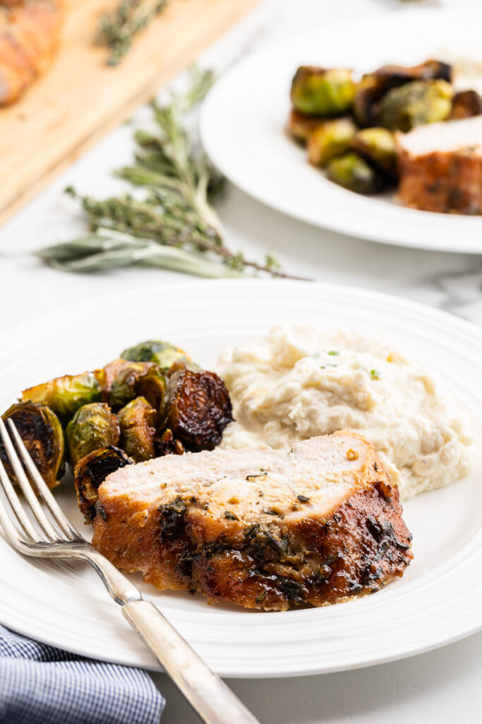 A slice of Keto Maple Mustard Roasted Turkey Breast on a white plate with roasted brussels sprouts and mashed cauliflower.