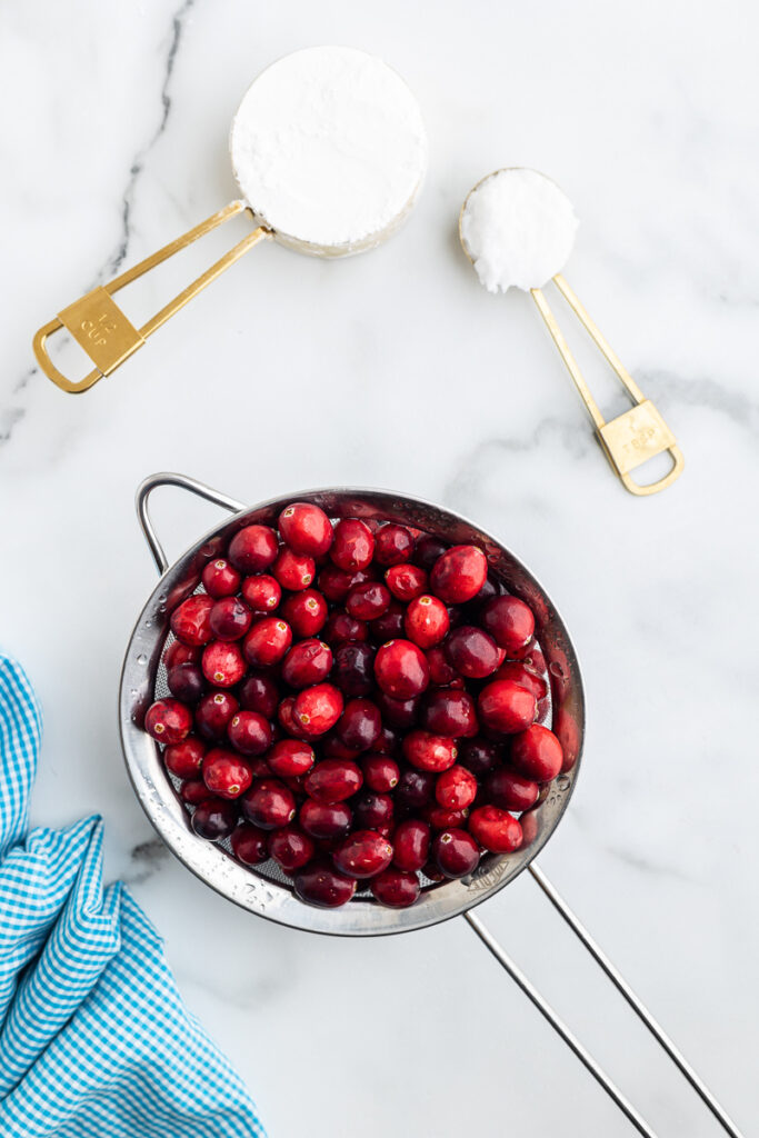 Overhead view of the ingredients needed to make Sugar-Free Dried Cranberries on a white marble counter.