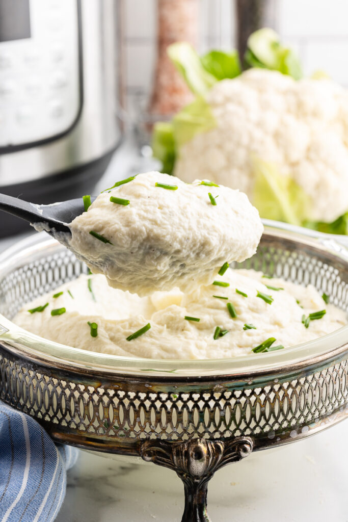 A serving spoon full of Creamy Garlic Mashed Cauliflower over the serving bowl full.