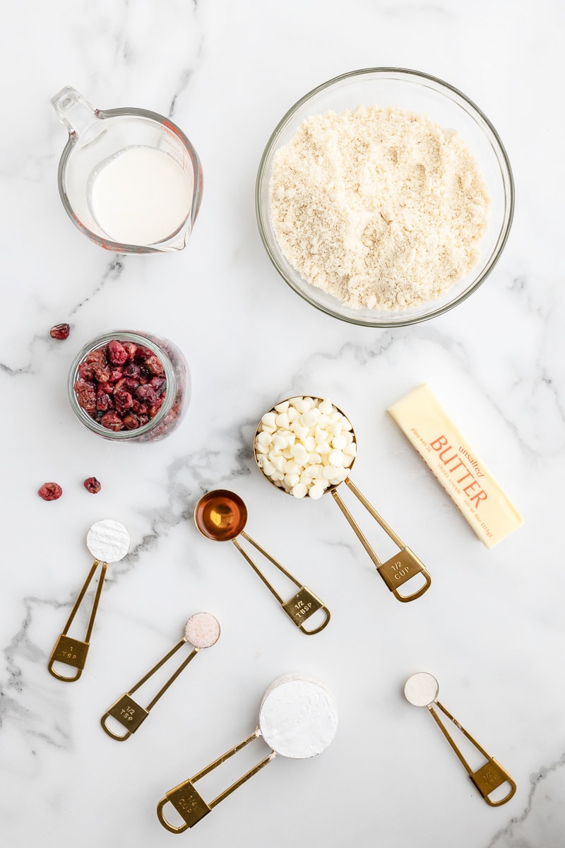 Overhead view of the ingredients needed to make keto white chocolate cranberry cookies on a white marble counter.
