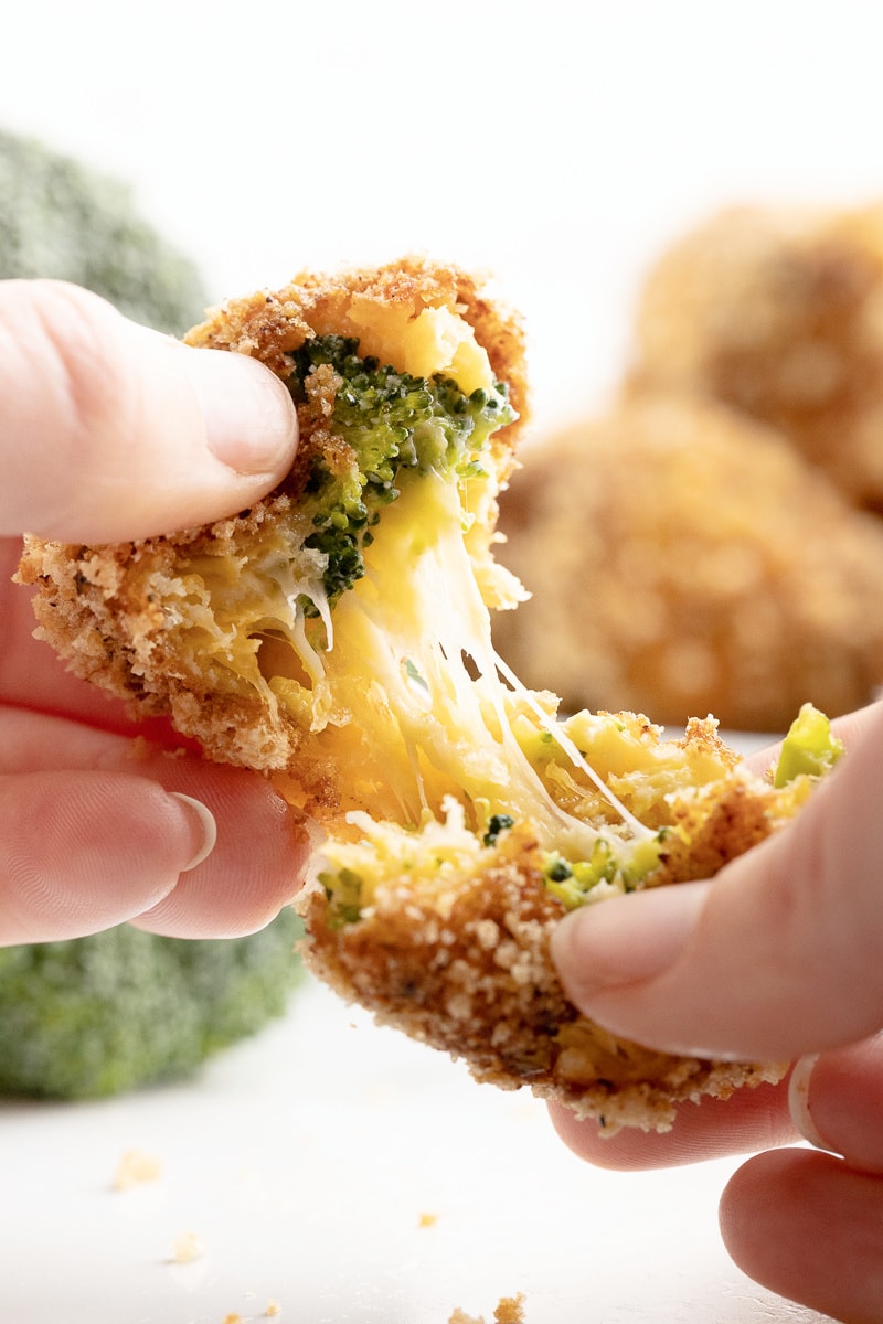 A white female presenting hand tearing open a keto broccoli cheese ball and showing a gooey cheese pull.